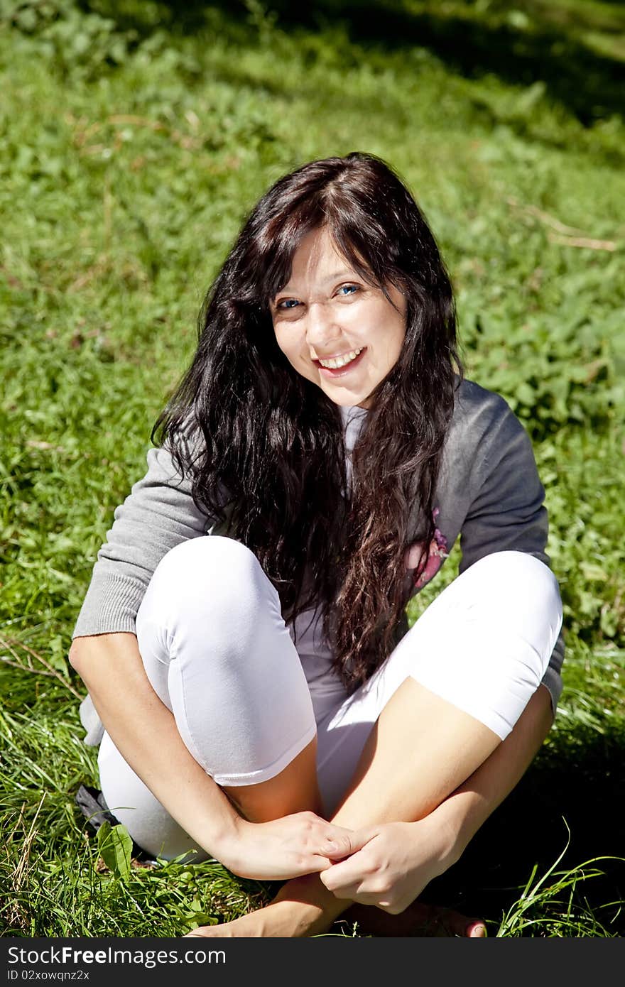 Portrait of beautiful brunette girl with blue eyes on green grass in the park. Portrait of beautiful brunette girl with blue eyes on green grass in the park.