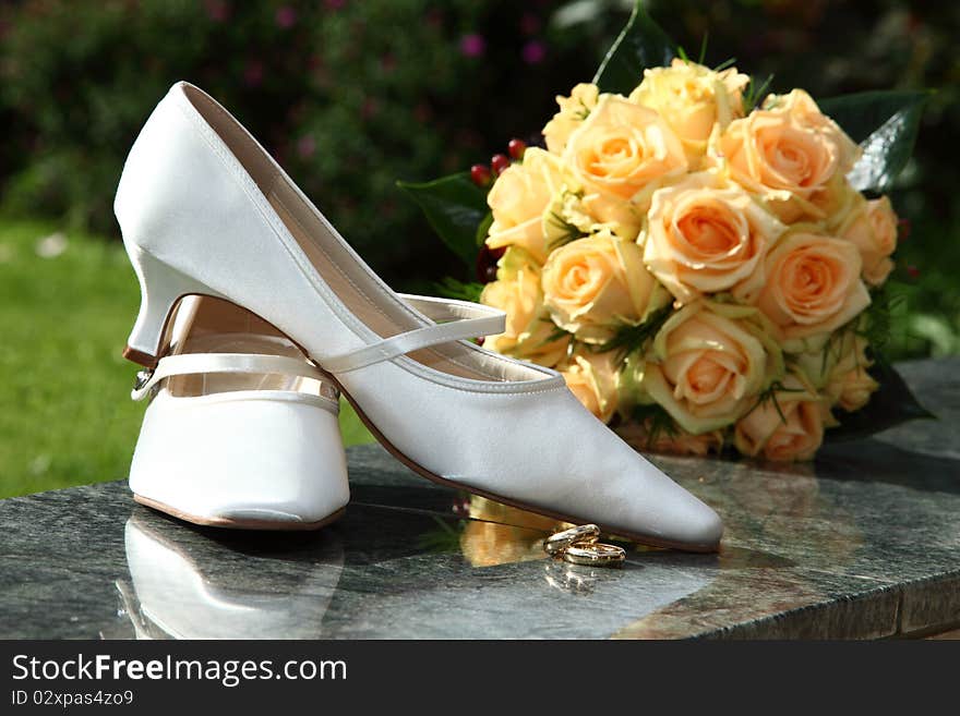 Engagement - shoes with orange rose bouquet and white bridal shoes and golden rings. focus is on rings and shoes. Engagement - shoes with orange rose bouquet and white bridal shoes and golden rings. focus is on rings and shoes