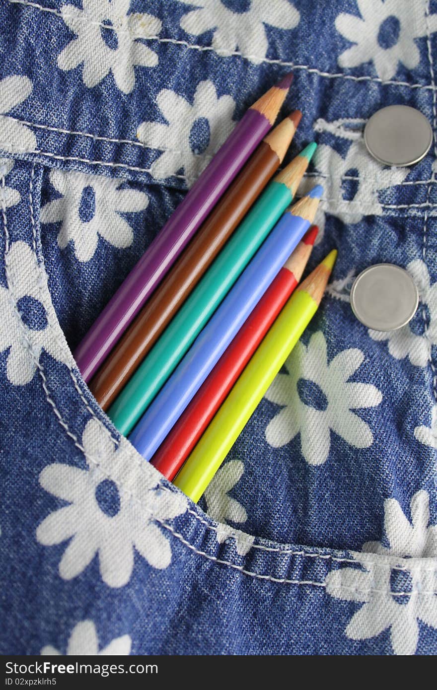 Colored pencils lined up in the pocket of cute denim overalls. Colored pencils lined up in the pocket of cute denim overalls.