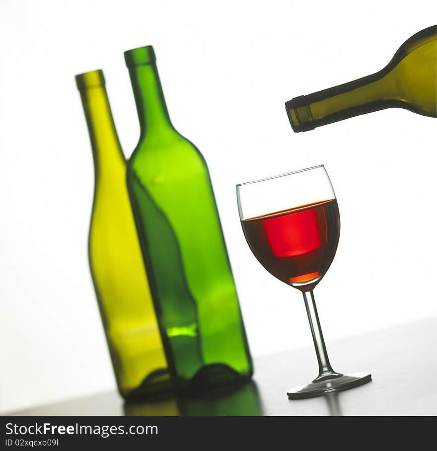 Glass of red wine with two green wine bottles