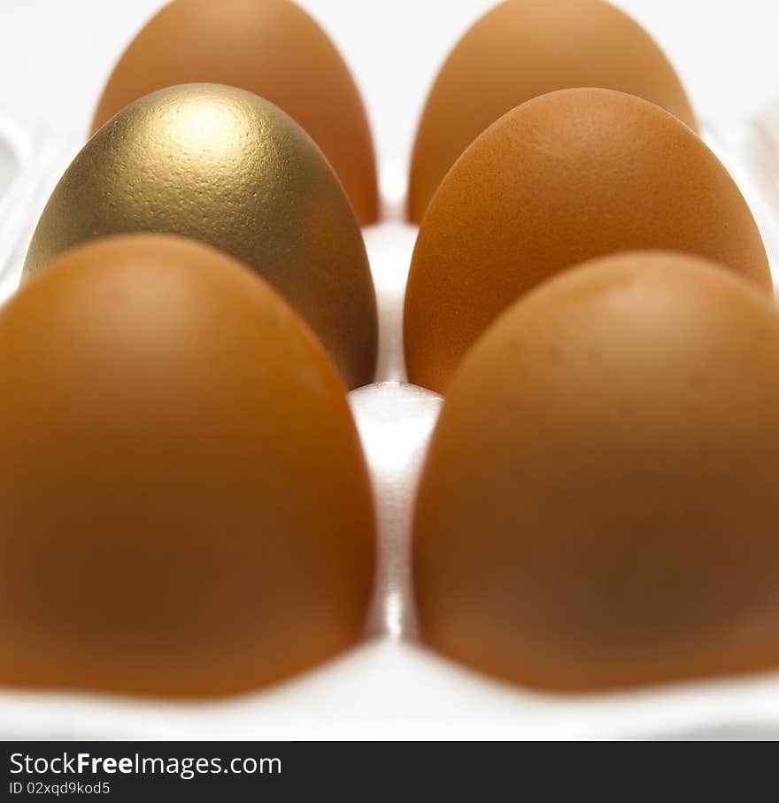 Close up of one gold and five brown eggs