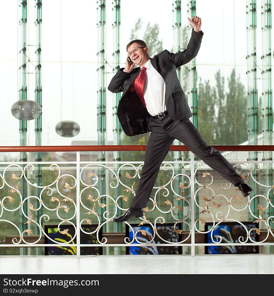 Smiling jumping man with mobile phone on background of glass wall