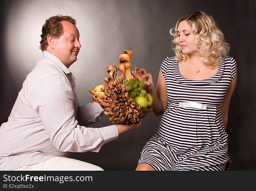 Photo of family pair with the basket of fruit. A woman is pregnant