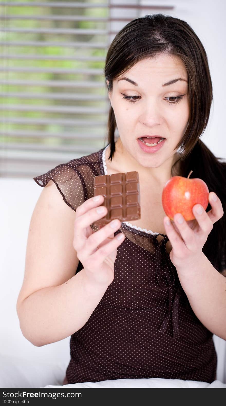 Young adult brunette woman in bed with chocolate and apple