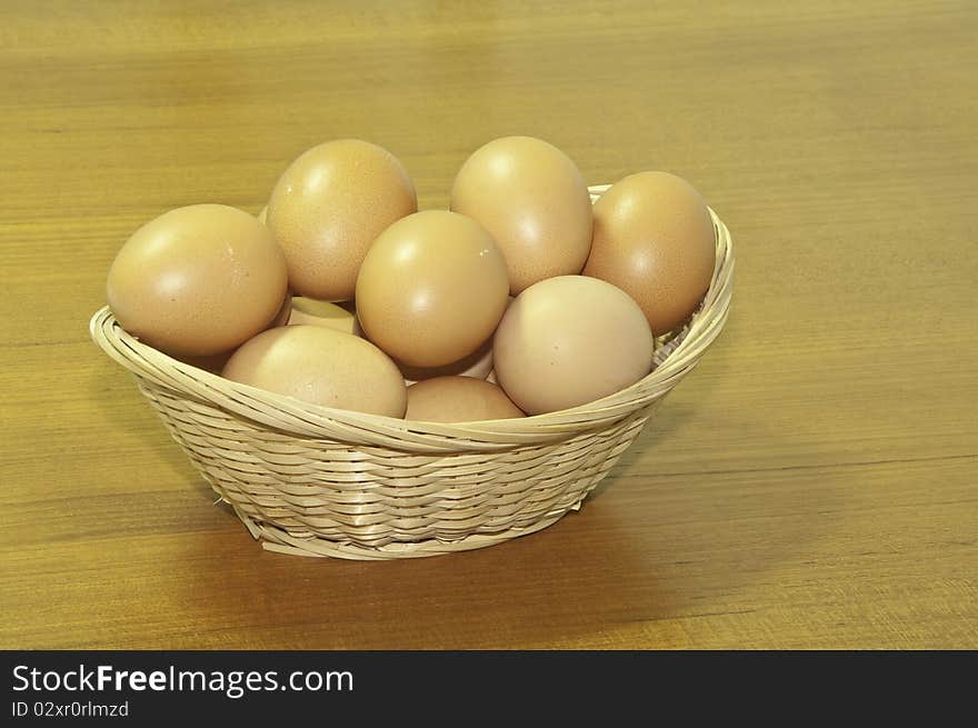 This image shows a wicker basket with chicken eggs on a wooden board. This image shows a wicker basket with chicken eggs on a wooden board