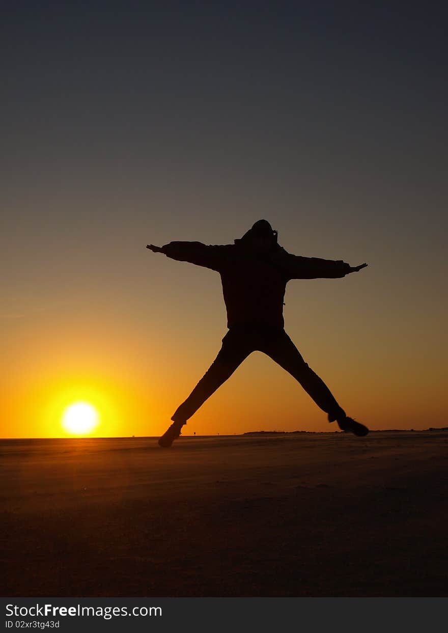 A person jumping in the air during sunset at a beach. A person jumping in the air during sunset at a beach