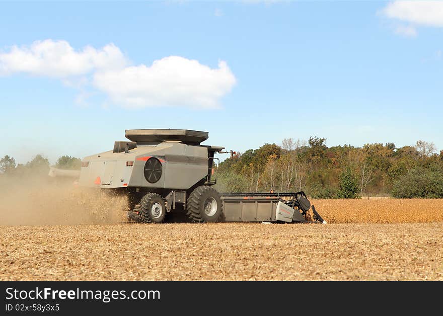 Combine in a farm field harvesting soybeans with a clear blue sky. Combine in a farm field harvesting soybeans with a clear blue sky