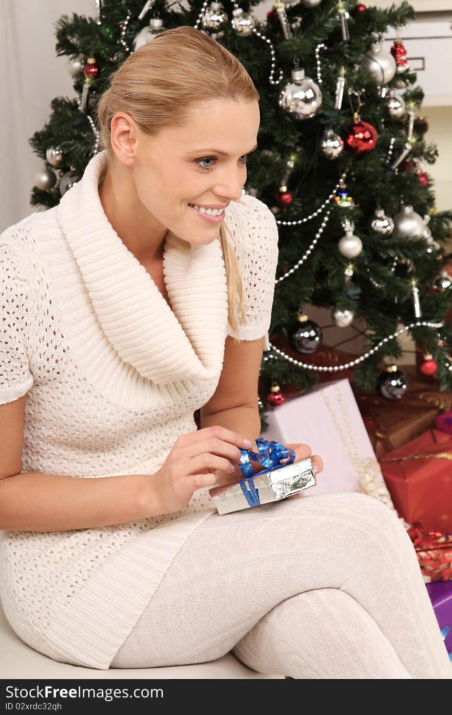 Beautiful blond woman sitting in front of a christmas-tree with a present. Beautiful blond woman sitting in front of a christmas-tree with a present