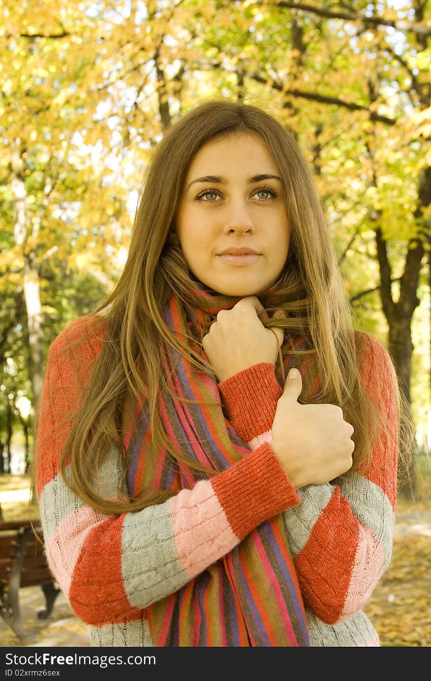 Autumn portrait of a beautiful young woman against yellow leaves. The girl was wrapped in a scarf