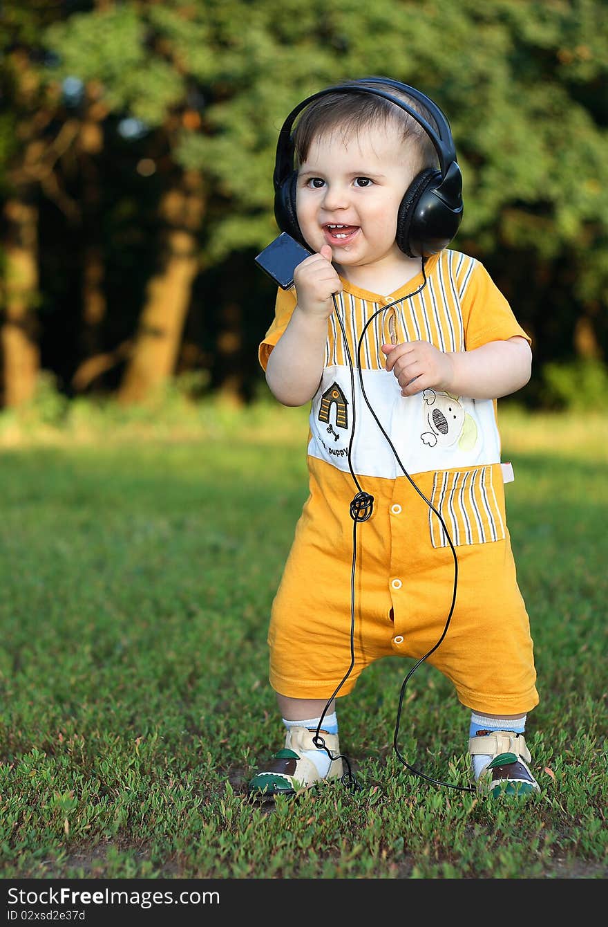 Little boy with headphones staying on the grass. He was smiling from ear to ear. From an open mouth, stick out teeth. Little boy with headphones staying on the grass. He was smiling from ear to ear. From an open mouth, stick out teeth.