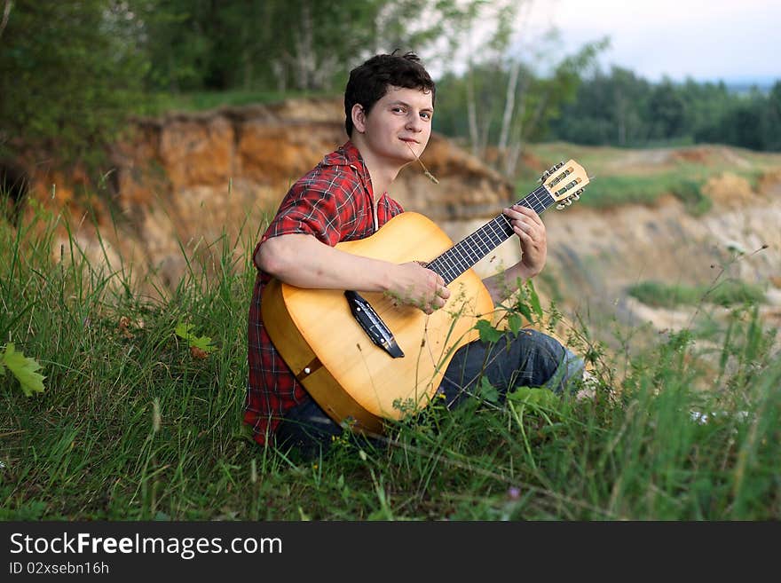 A lone young man with a guitar on a precipice with grass in his mouth. A lone young man with a guitar on a precipice with grass in his mouth