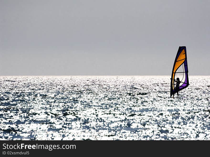 Silhouette of a windsurfer sailing at sunset