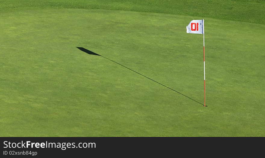 A flagpole and its shadow near the hole on a green golf field. A flagpole and its shadow near the hole on a green golf field.