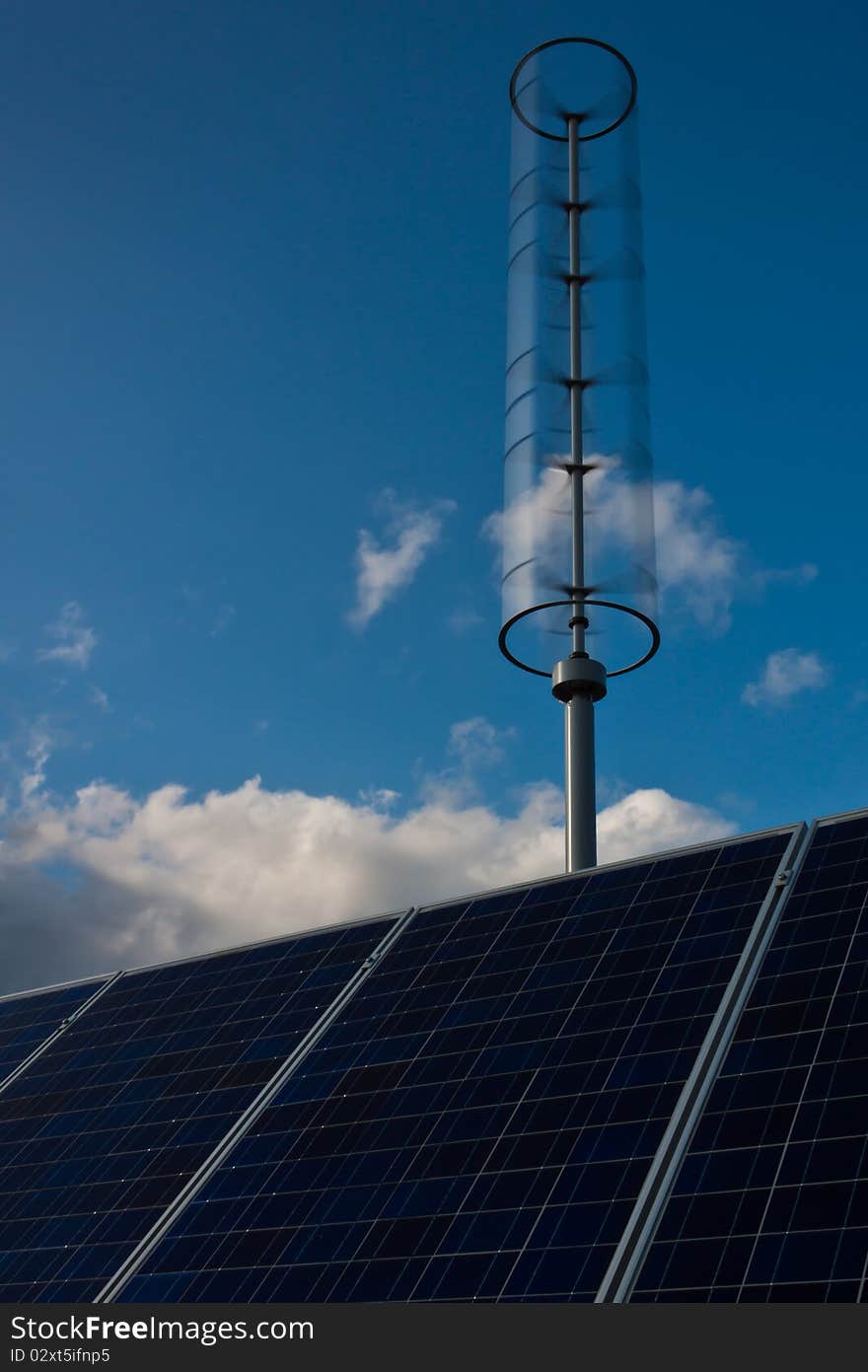 A vertical-axis turbine and solar panel array stand ready to gather green electricity. A vertical-axis turbine and solar panel array stand ready to gather green electricity.