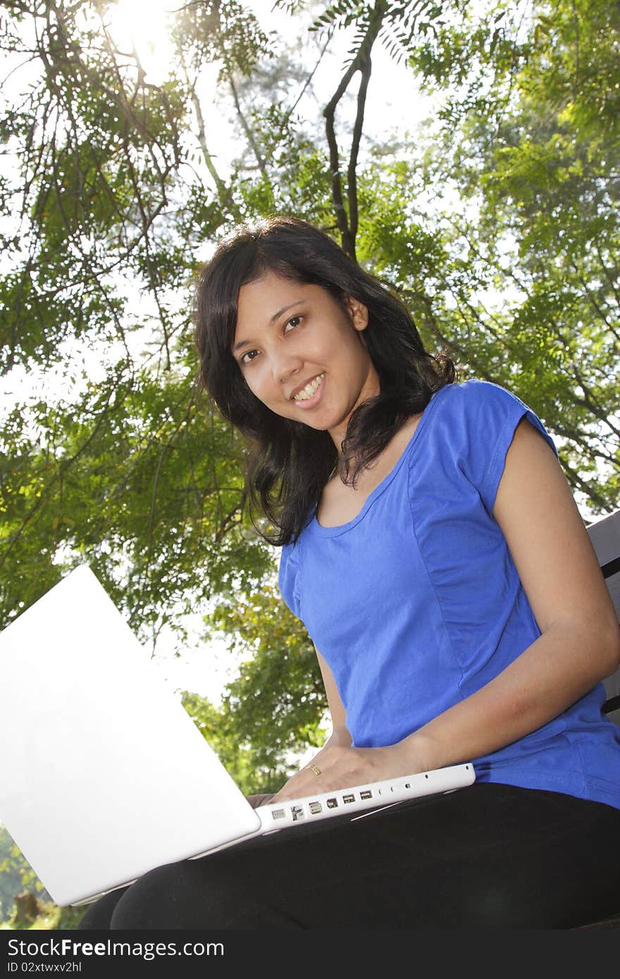 An Asian woman using her laptop on a park bench. An Asian woman using her laptop on a park bench