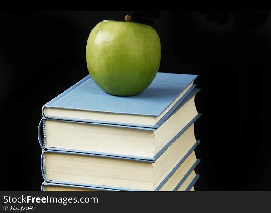 Green apple on on the stack of books isolated on black