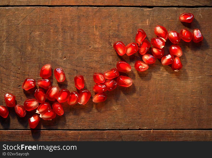 Lot of red pomegranate seeds lying in a row on dark wooden board