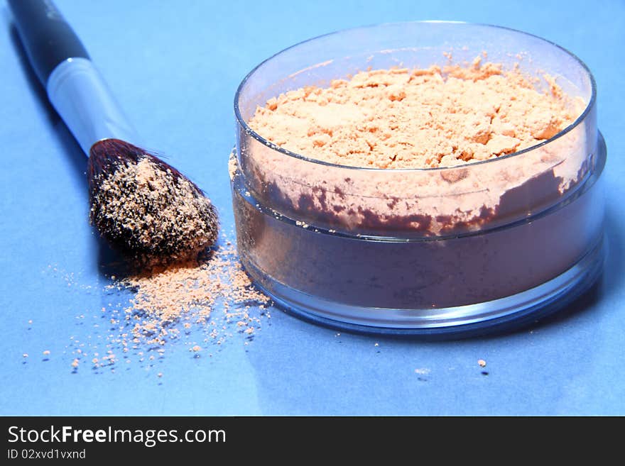 Loose powder on a blue background with the brush of natural bristles to apply it.