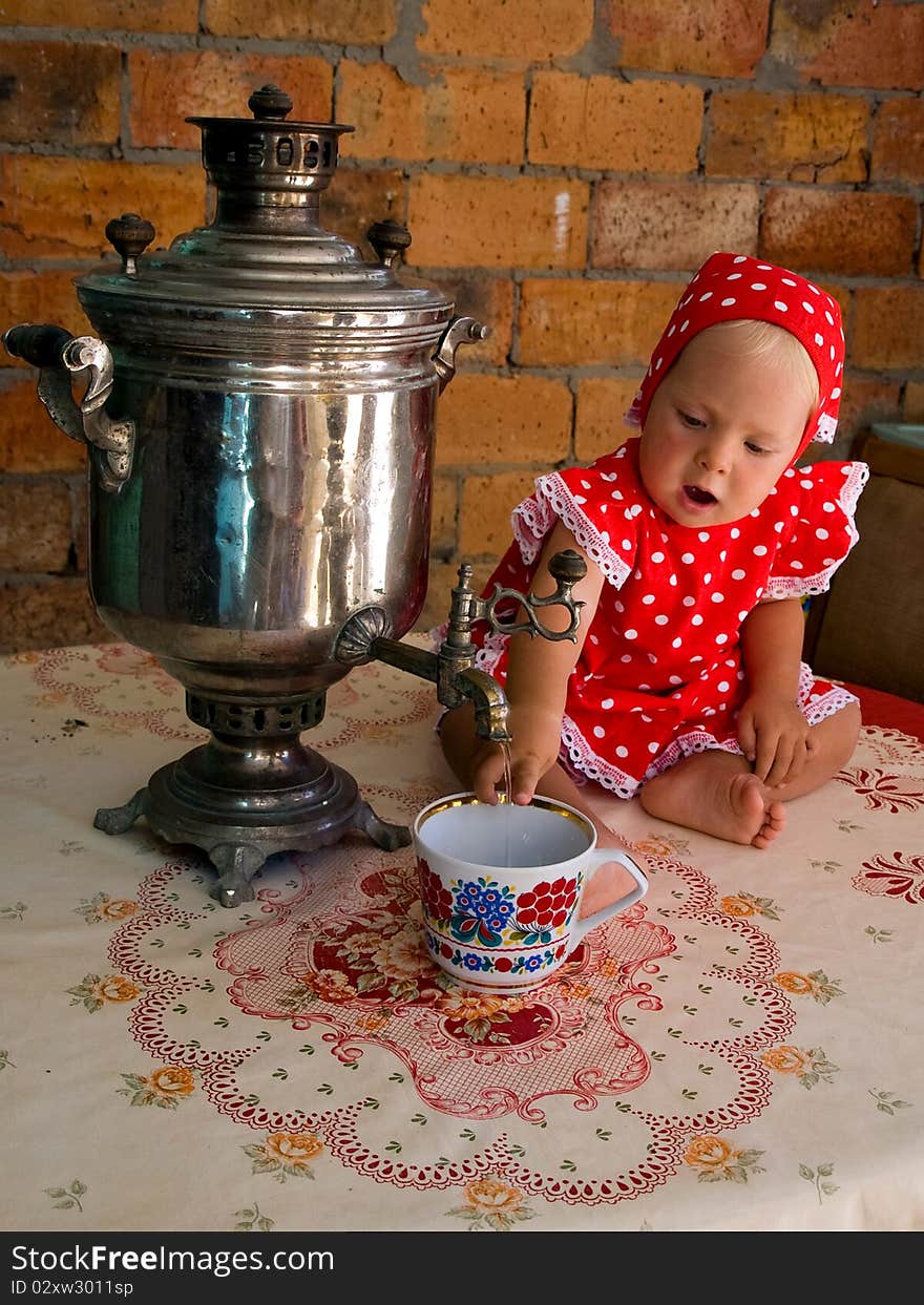 Little girl in a red polka-dot dress, with a samovar, sitting in front of a brick wall and pours water into a cup. Little girl in a red polka-dot dress, with a samovar, sitting in front of a brick wall and pours water into a cup