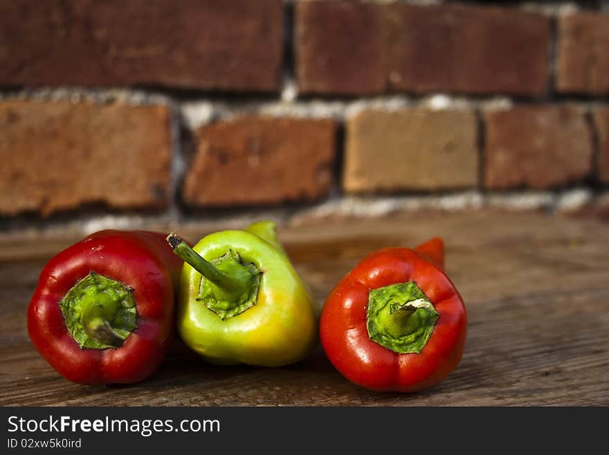 Three peppers on a wooden table with a red wall in the background.