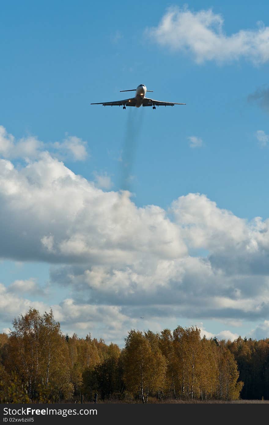 The photograph shows the aircraft, preparing to sit down at the airport. Frame is made against the backdrop of autumn forest and clouds. The photograph shows the aircraft, preparing to sit down at the airport. Frame is made against the backdrop of autumn forest and clouds.