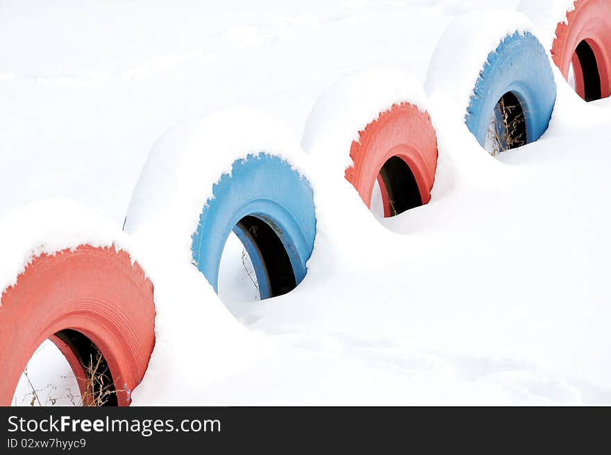 Colored tires on the playground covered with snow