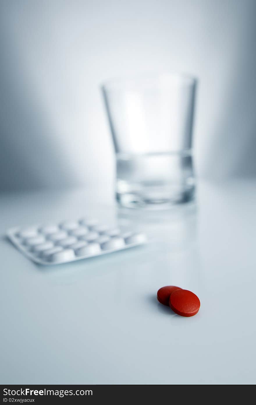 Medical red pill and aspirin with water and glass