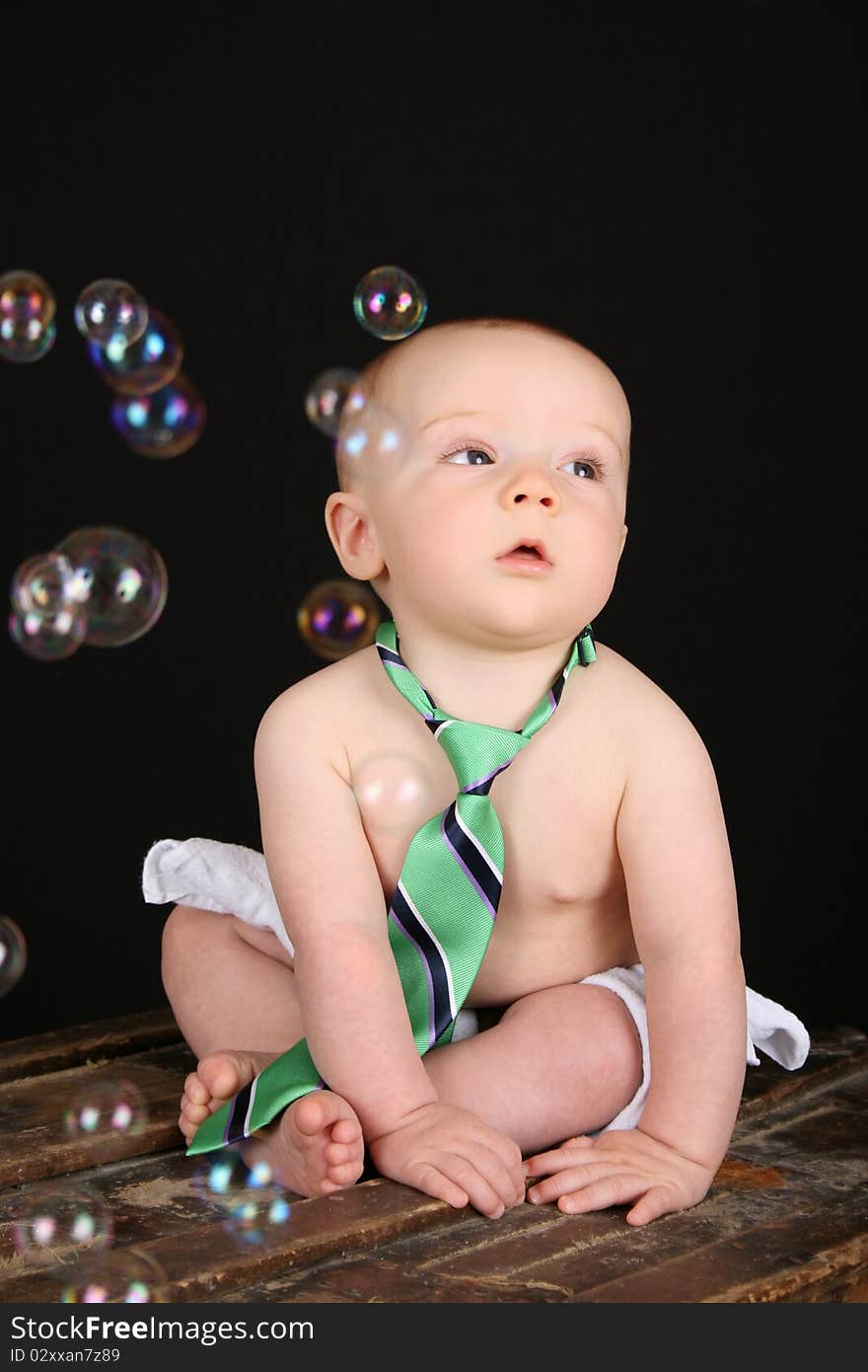 Cute baby boy sitting on an antique trunk looking at bubbles. Cute baby boy sitting on an antique trunk looking at bubbles