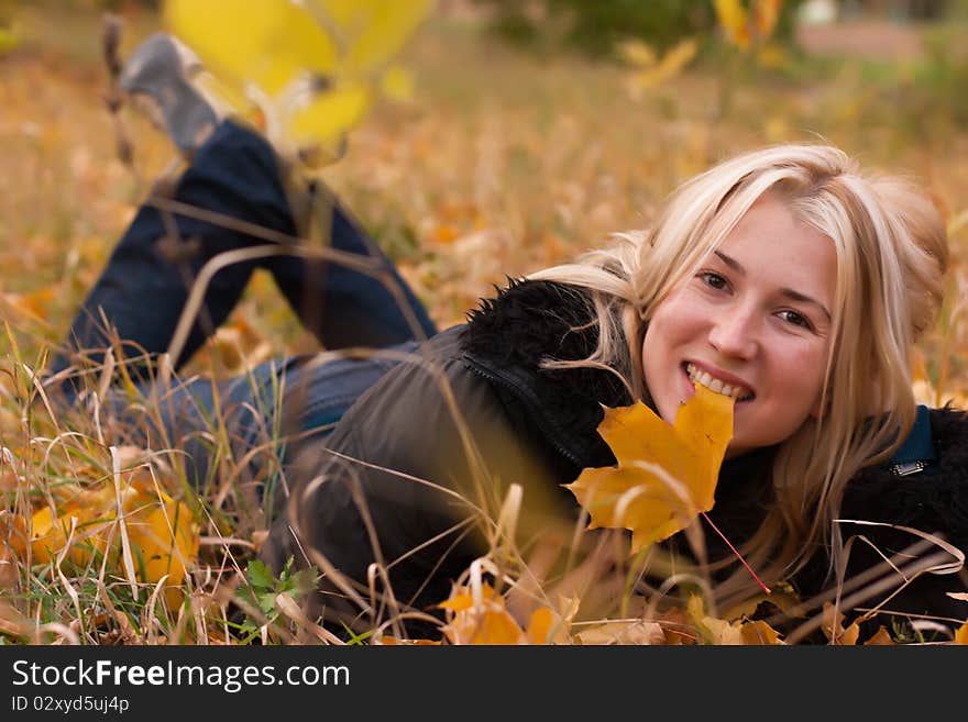 Beautiful young woman lying on autumn leaves with maple leaf in her mouth. Beautiful young woman lying on autumn leaves with maple leaf in her mouth