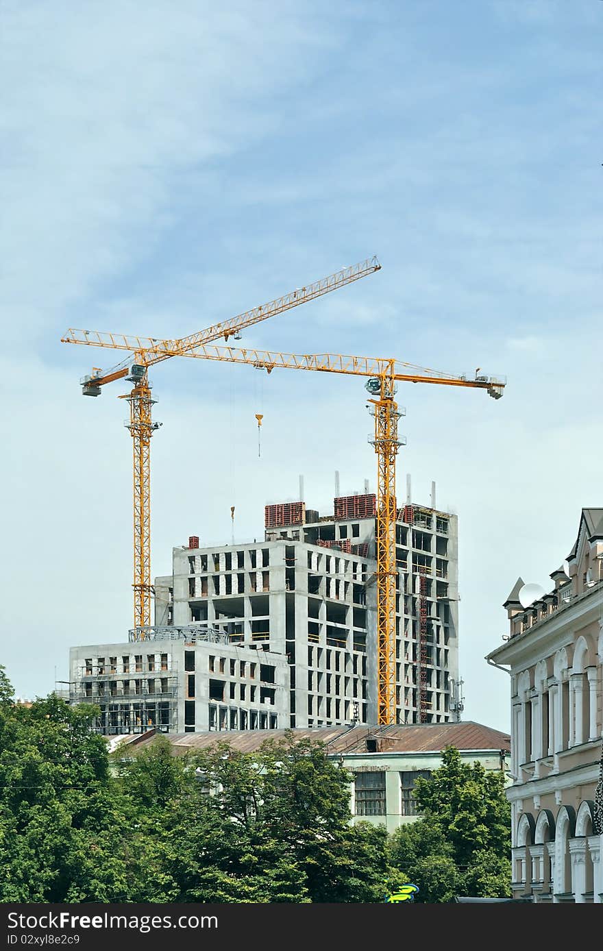 In the historical part of the one of the Ukrainian towns builds modern habitant and office houses. One can see two hoisting cranes against blue sky. In the historical part of the one of the Ukrainian towns builds modern habitant and office houses. One can see two hoisting cranes against blue sky.