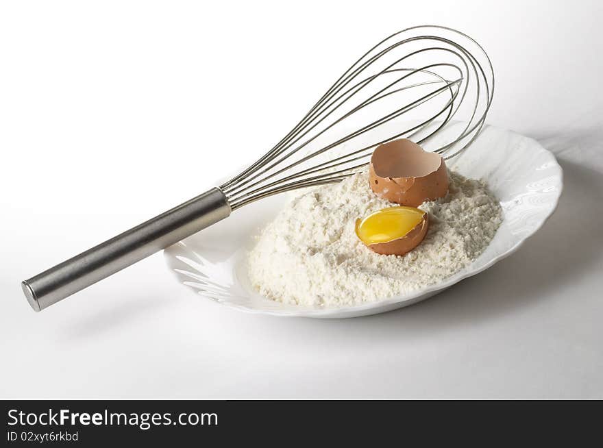 Flour pile, egg and metal whisker over gray gradient background. Flour pile, egg and metal whisker over gray gradient background