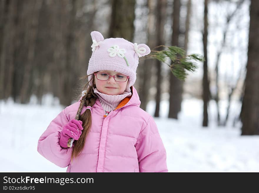 Adorable winter small girl in glasses and pink hat and jacket in the forest