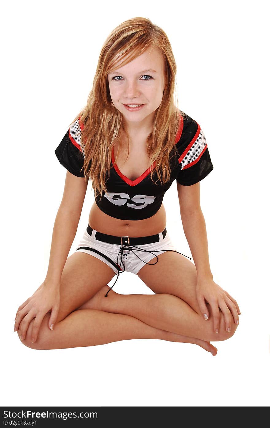 A young teenage soccer girl sitting on the floor in her uniform, with her legs crossed, for a portrait in the studio, over white background. A young teenage soccer girl sitting on the floor in her uniform, with her legs crossed, for a portrait in the studio, over white background.