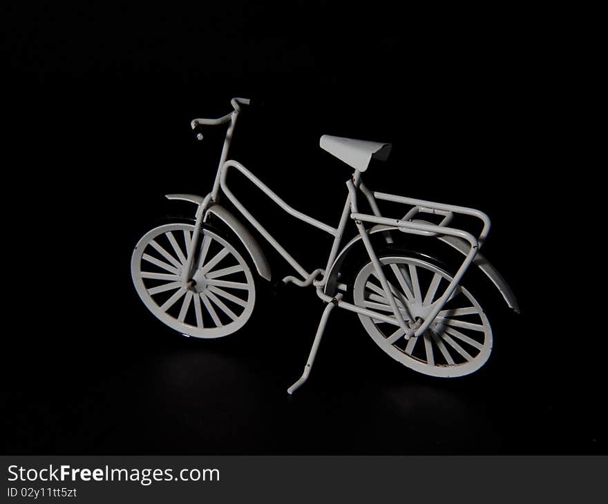 A white metal miniature bike on a black background, a little worn object. A white metal miniature bike on a black background, a little worn object