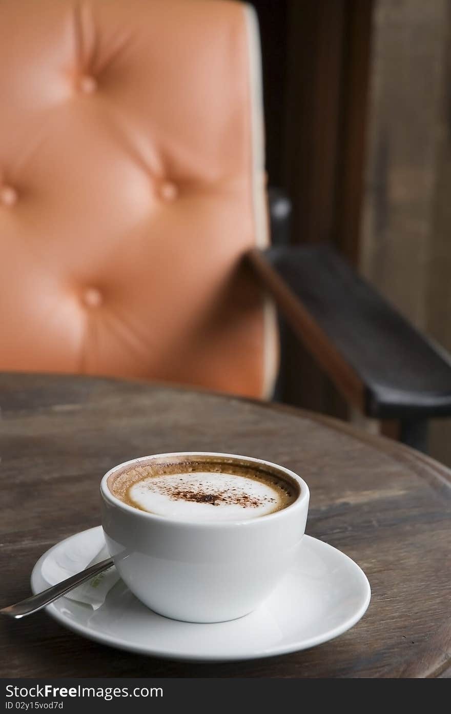 A cup of Cappuccino on wooden table with orange armchair background. A cup of Cappuccino on wooden table with orange armchair background