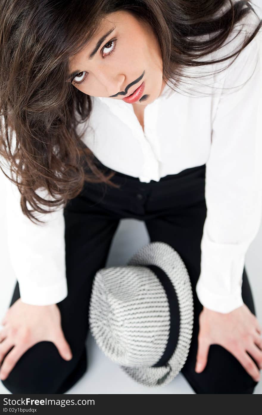 Beautiful girl with moustache dandy makeup sitting with hat, looking up at camera. Beautiful girl with moustache dandy makeup sitting with hat, looking up at camera