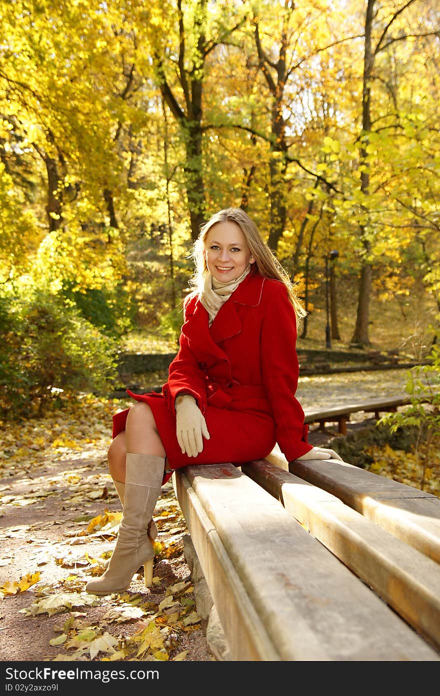 Beautiful girl in a red coat on a park bench