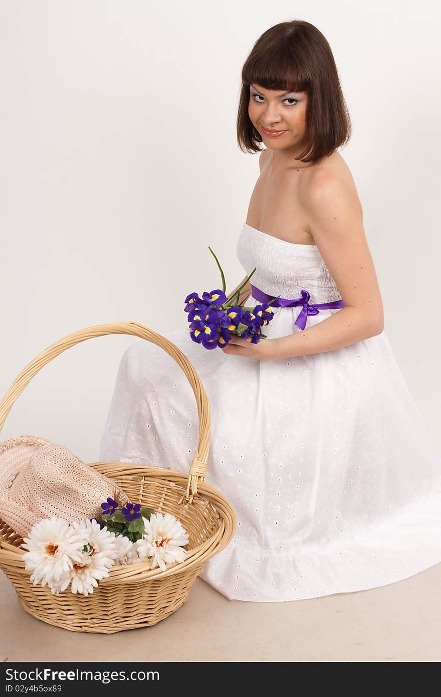 Beautiful girl holding a bouquet of irises and a basket, which is a hat and a bouquet of white flowers. She is in studio isolated on a white background. Beautiful girl holding a bouquet of irises and a basket, which is a hat and a bouquet of white flowers. She is in studio isolated on a white background