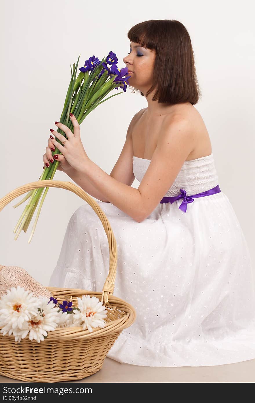 Beautiful girl holding a bouquet of irises and a basket, which is a hat and a bouquet of white flowers. She is in studio isolated on a white background. Beautiful girl holding a bouquet of irises and a basket, which is a hat and a bouquet of white flowers. She is in studio isolated on a white background