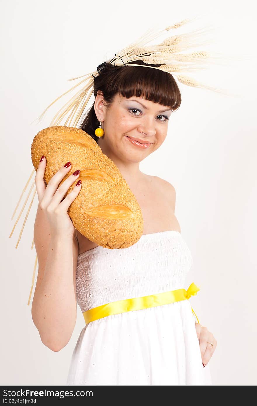 Beautiful brunette girl with ears of wheat in her hair is eating a bread isolated on the white background. Beautiful brunette girl with ears of wheat in her hair is eating a bread isolated on the white background