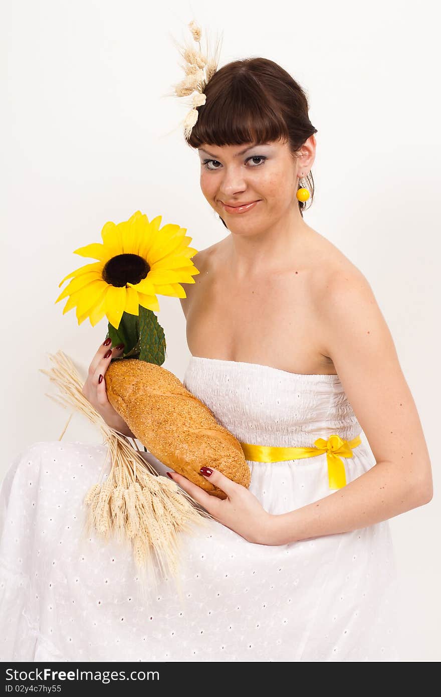 Beautiful brunette girl with sunflower and ears of wheat in her hair is eating a bread isolated on the white background. Beautiful brunette girl with sunflower and ears of wheat in her hair is eating a bread isolated on the white background