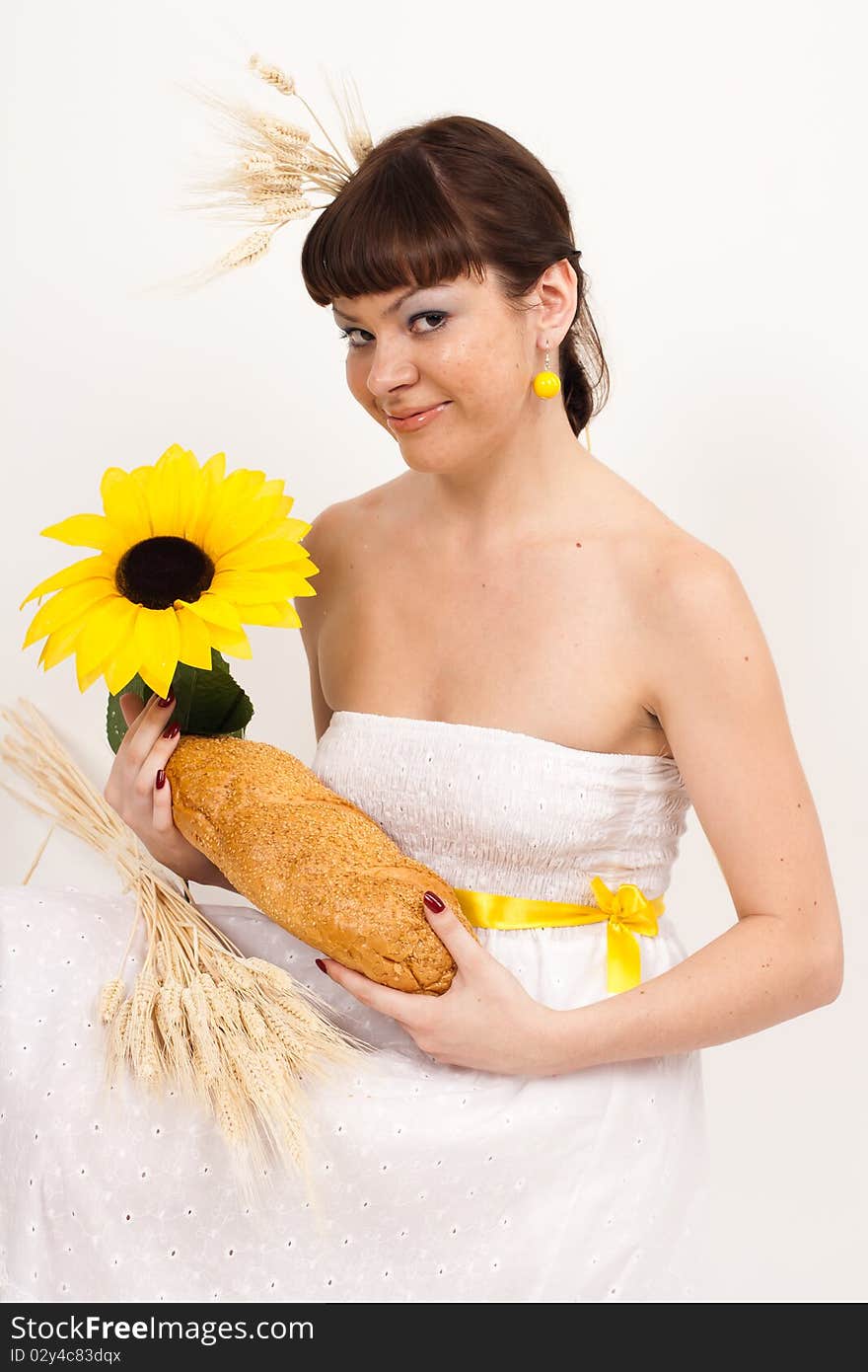 Beautiful brunette girl with sunflower and ears of wheat in her hair is eating a bread isolated on the white background. Beautiful brunette girl with sunflower and ears of wheat in her hair is eating a bread isolated on the white background