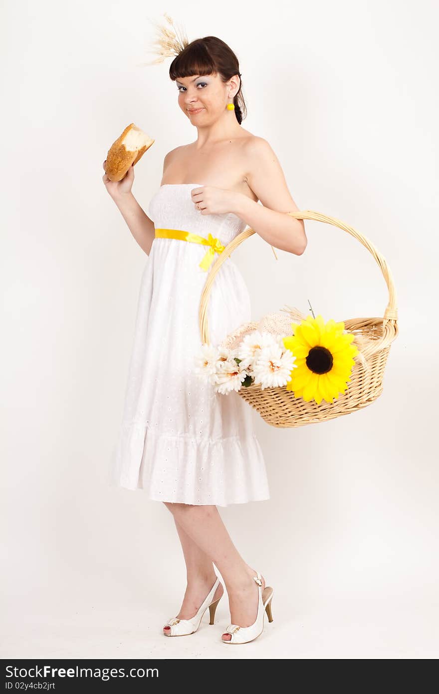 Beautiful brunette girl with sunflower and ears of wheat in her hair is eating a bread isolated on the white background. Beautiful brunette girl with sunflower and ears of wheat in her hair is eating a bread isolated on the white background