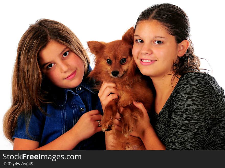 A young teen and her preteen sister loving on a Pomeranian puppy. Isolated on white. A young teen and her preteen sister loving on a Pomeranian puppy. Isolated on white.