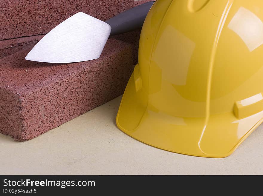 Yellow hard hat next to bricks and a stonemason's tool.