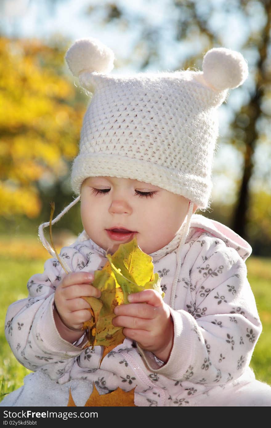 Baby with maple leaf in the hand playing in the park. Baby with maple leaf in the hand playing in the park