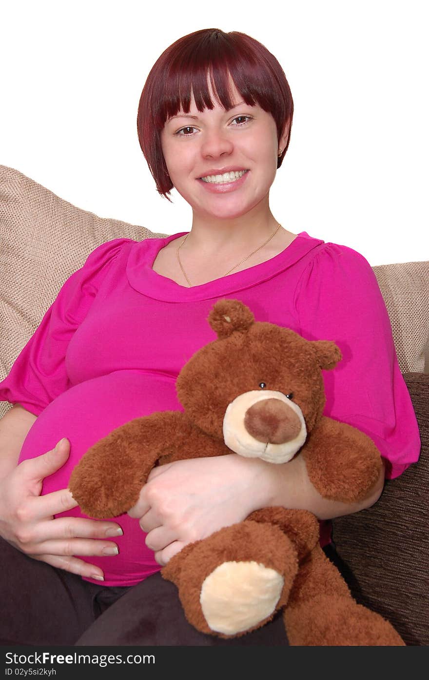 Happy young pregnant woman sitting on the sofa with teddy