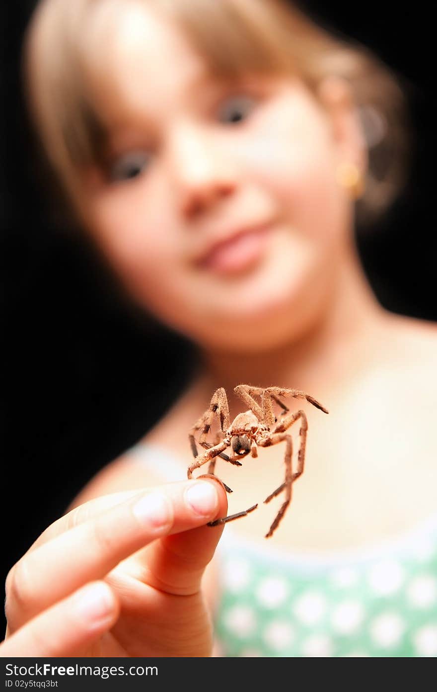 Girl holding brown spider by one leg and looking s