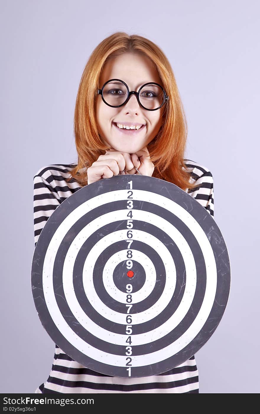 Red-haired girl with dartboard. Studio shot.