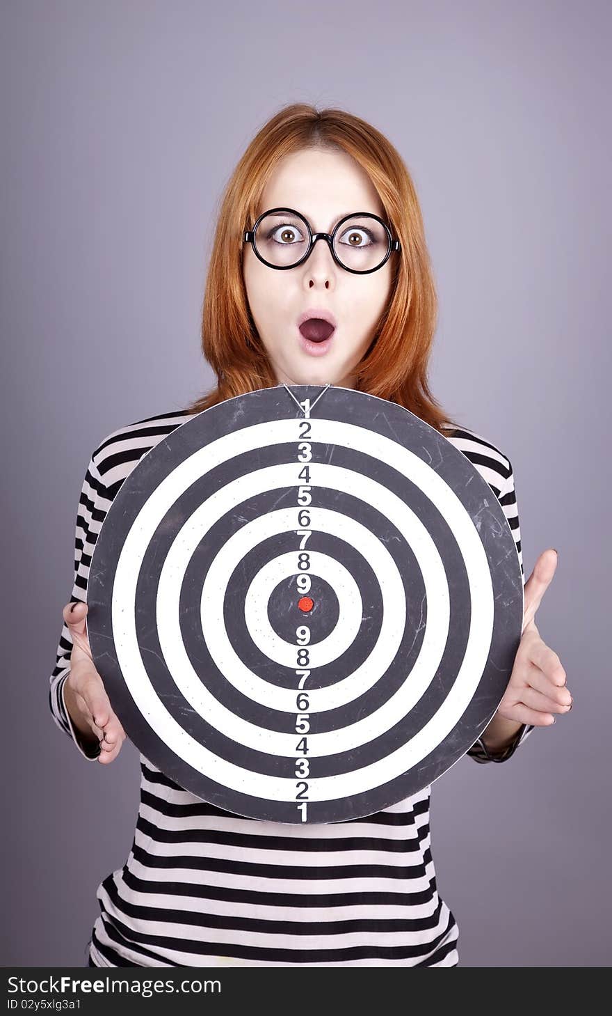 Red-haired girl with dartboard. Studio shot.